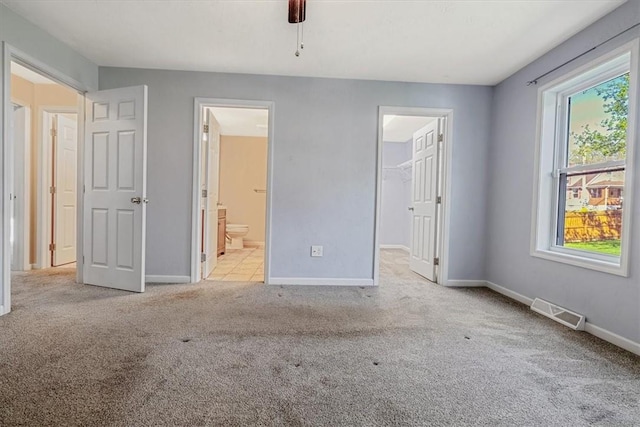 unfurnished bedroom featuring carpet flooring, a walk in closet, ensuite bath, baseboards, and visible vents