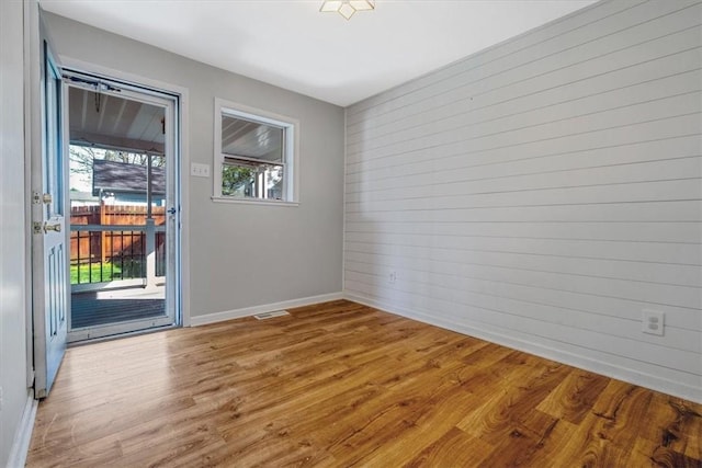 unfurnished room featuring visible vents, wood walls, baseboards, and wood finished floors