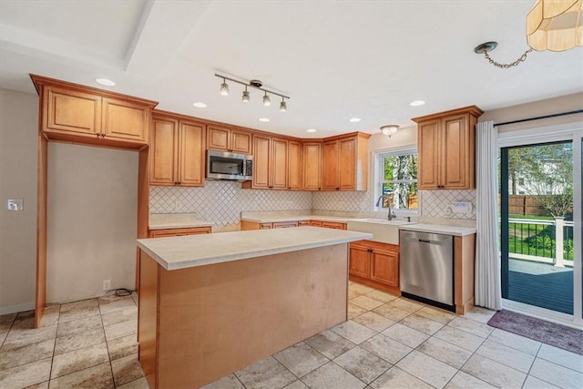 kitchen with a kitchen island, light countertops, a sink, appliances with stainless steel finishes, and backsplash