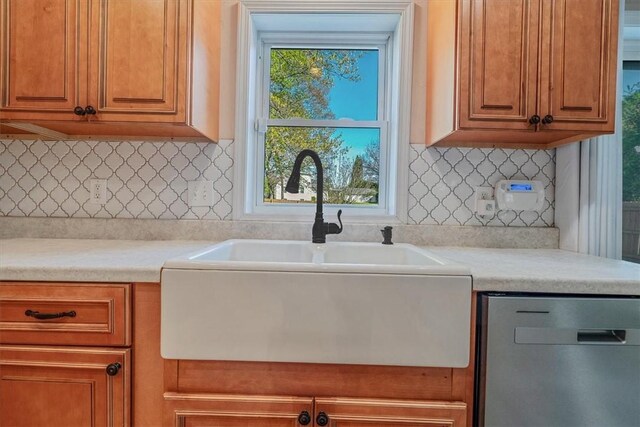 kitchen featuring stainless steel dishwasher, a sink, brown cabinets, and light countertops