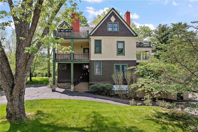 back of house with a lawn, a chimney, and a balcony