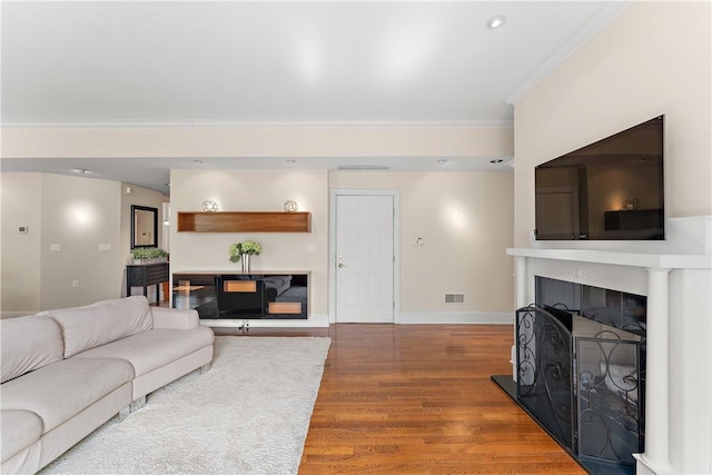 living room featuring a fireplace, baseboards, wood finished floors, visible vents, and ornamental molding
