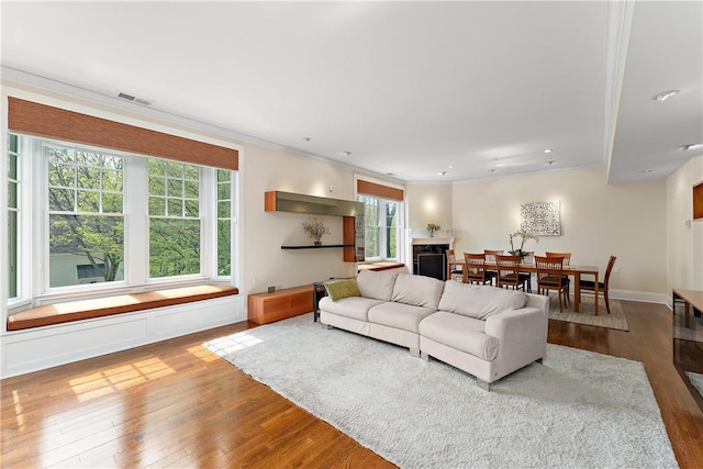 living room featuring plenty of natural light, ornamental molding, visible vents, and hardwood / wood-style floors