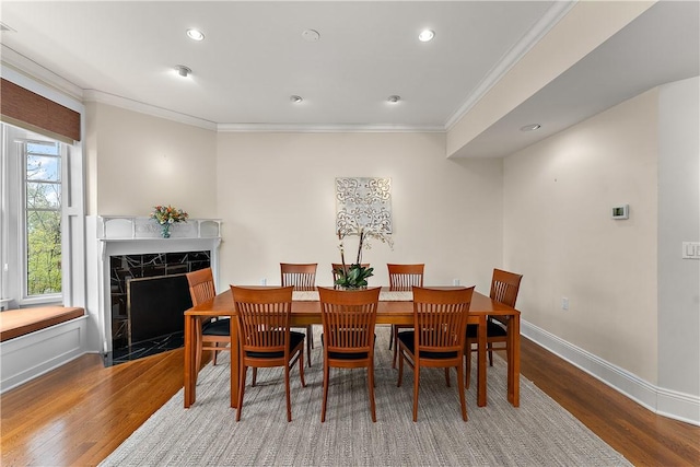 dining room featuring crown molding, a high end fireplace, wood finished floors, baseboards, and recessed lighting