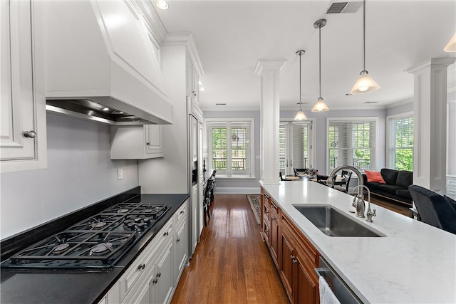 kitchen with brown cabinets, a sink, decorative columns, visible vents, and custom exhaust hood