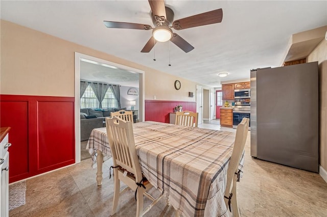 dining space with ceiling fan and a wainscoted wall