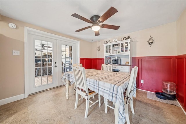 dining room featuring a wainscoted wall, ceiling fan, french doors, and a decorative wall