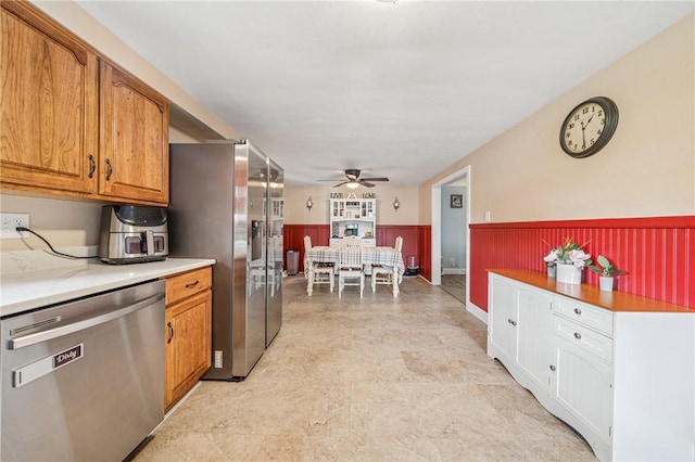 kitchen with a ceiling fan, wainscoting, brown cabinets, light countertops, and stainless steel appliances
