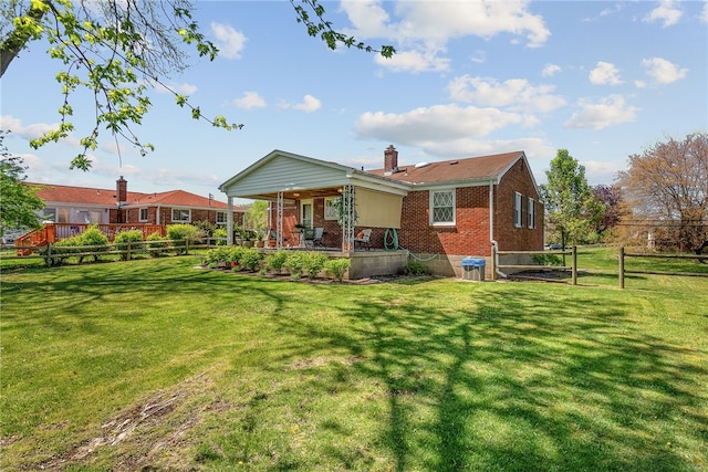 back of property featuring brick siding, a lawn, fence, and a chimney