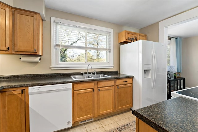 kitchen with visible vents, dark countertops, a sink, light tile patterned floors, and white appliances
