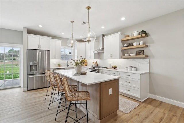kitchen with wall chimney range hood, a breakfast bar area, appliances with stainless steel finishes, tasteful backsplash, and open shelves