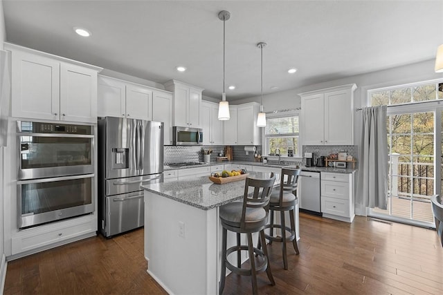 kitchen with decorative backsplash, dark wood-style flooring, a kitchen island, white cabinets, and stainless steel appliances