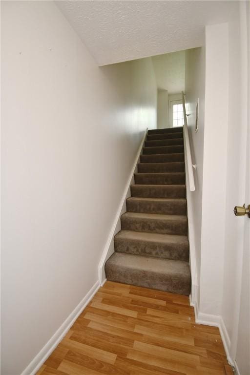 stairs with baseboards, a textured ceiling, and wood finished floors