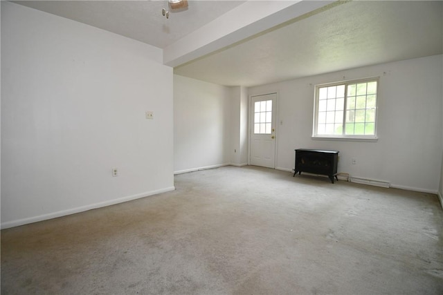 carpeted spare room featuring baseboards, a baseboard heating unit, and a wood stove