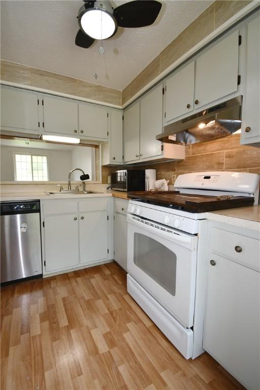 kitchen featuring white gas range, light wood-type flooring, under cabinet range hood, a sink, and dishwasher