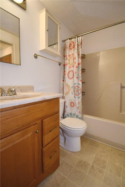 full bath featuring vanity, toilet, a textured ceiling, and shower / tub combo with curtain