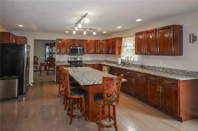 kitchen with a sink, a center island, stainless steel appliances, light wood-type flooring, and a kitchen bar