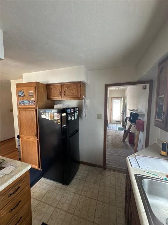 kitchen featuring a sink, light countertops, brown cabinetry, freestanding refrigerator, and baseboards