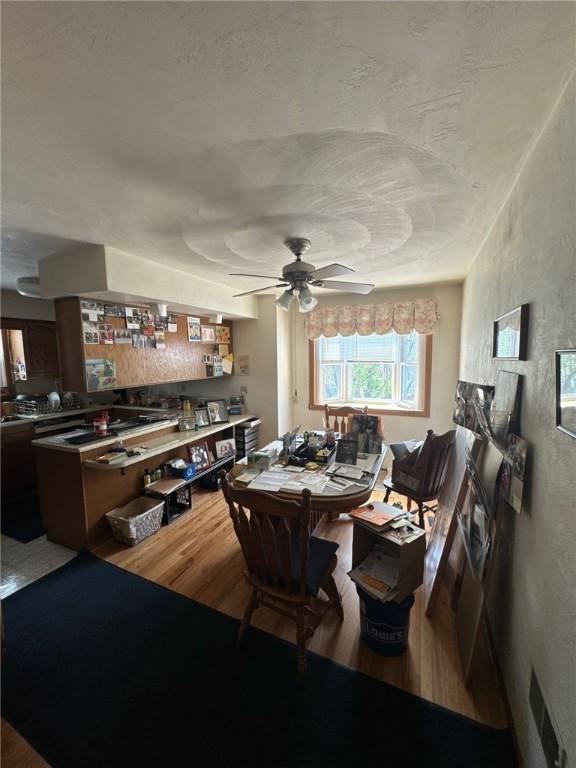 dining area featuring a ceiling fan, a textured wall, visible vents, and wood finished floors