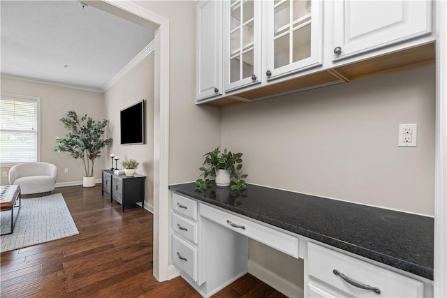 interior space featuring baseboards, ornamental molding, built in desk, and dark wood-type flooring