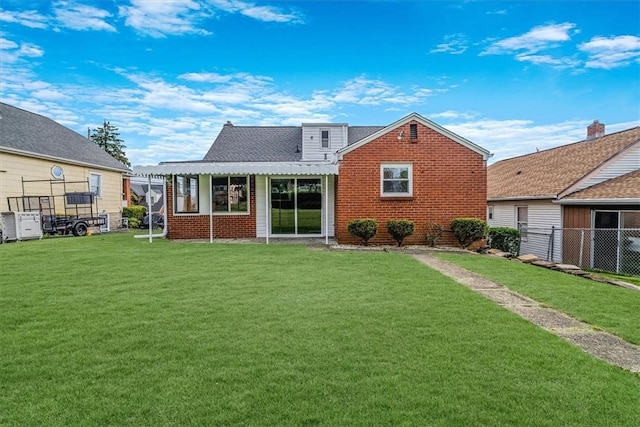 rear view of property with fence, a yard, and brick siding