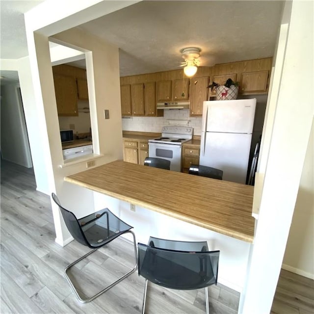 kitchen with tasteful backsplash, brown cabinets, wood finished floors, under cabinet range hood, and white appliances