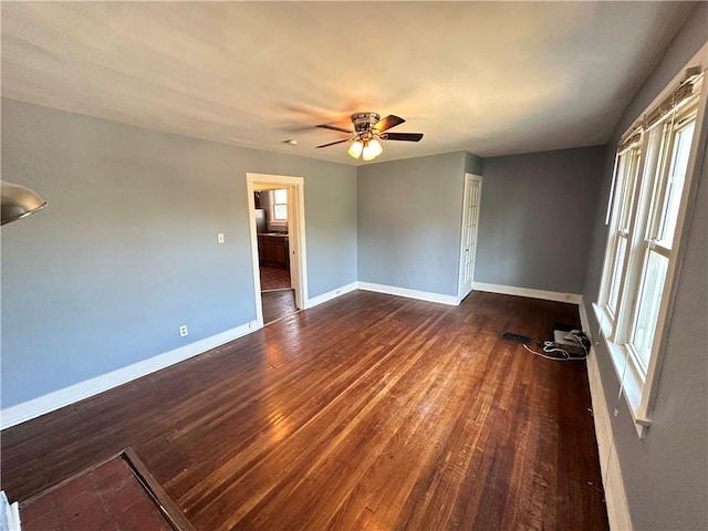 empty room with a ceiling fan, baseboards, and dark wood finished floors