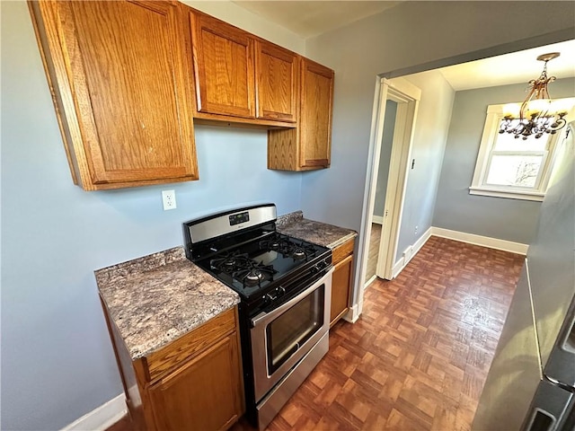 kitchen featuring an inviting chandelier, stainless steel gas stove, brown cabinetry, dark stone countertops, and baseboards