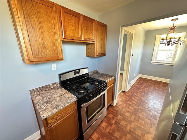 kitchen featuring a notable chandelier, stainless steel gas range oven, brown cabinetry, dark stone countertops, and baseboards