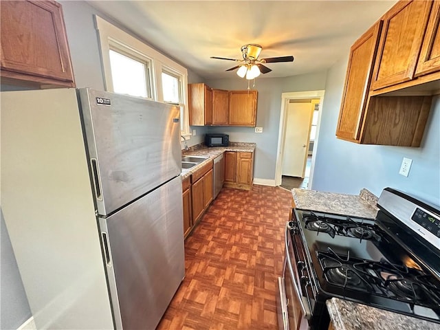 kitchen featuring ceiling fan, brown cabinetry, appliances with stainless steel finishes, a sink, and baseboards