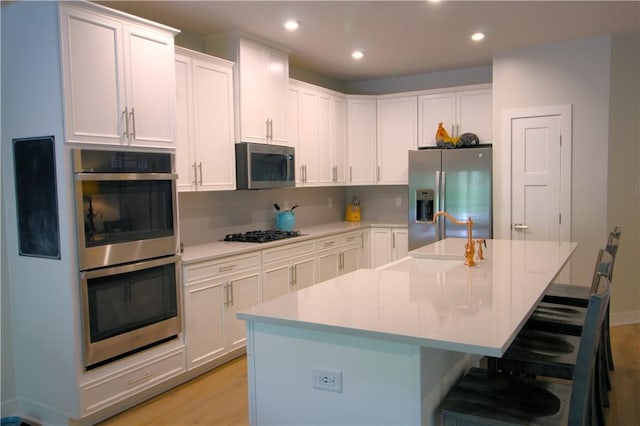 kitchen featuring a sink, light wood-style floors, a kitchen breakfast bar, stainless steel appliances, and white cabinetry