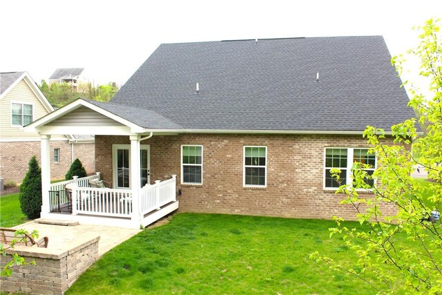 back of house featuring brick siding, a shingled roof, a patio area, and a yard