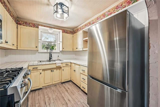 kitchen featuring tile countertops, a sink, appliances with stainless steel finishes, and cream cabinets