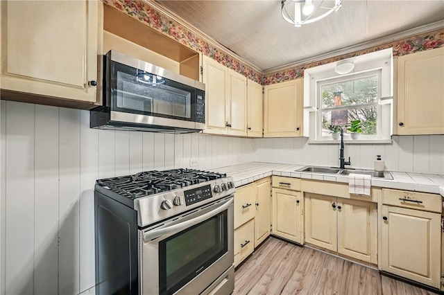kitchen with stainless steel appliances, tile counters, cream cabinetry, and a sink