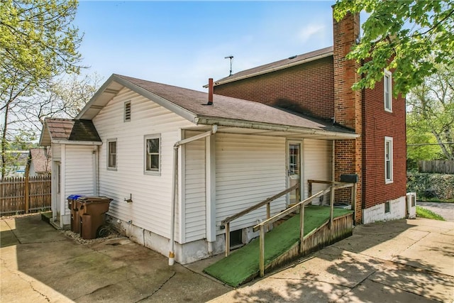 rear view of house featuring a patio, a shingled roof, fence, and a chimney