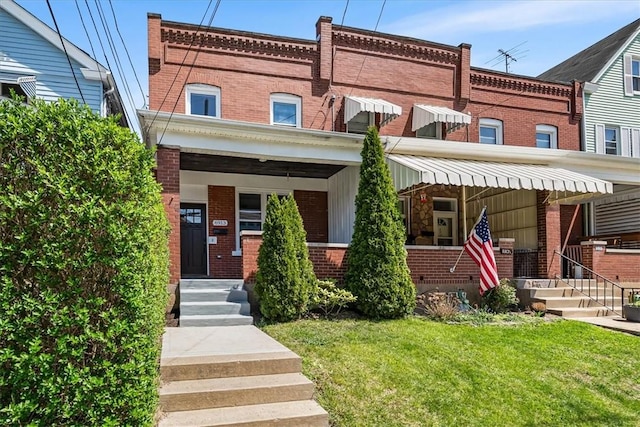 view of front facade with brick siding, a front lawn, and covered porch