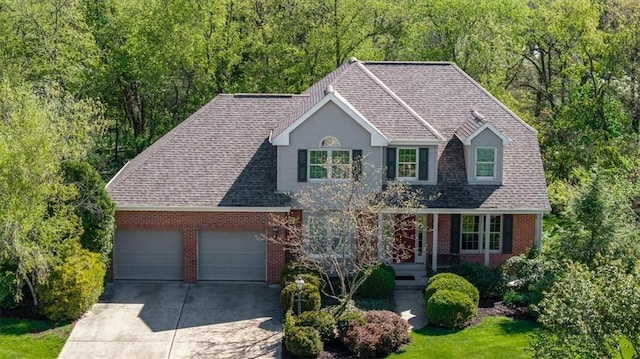 traditional-style home with a shingled roof, brick siding, a garage, driveway, and a wooded view