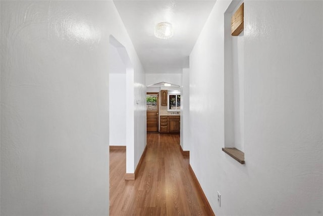 hall with baseboards, arched walkways, and wood finished floors