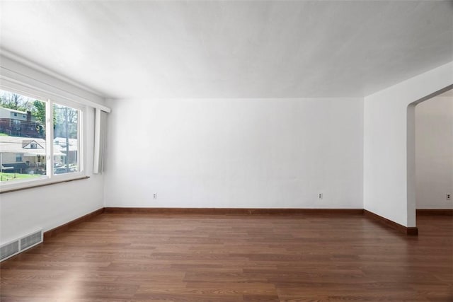 unfurnished room with visible vents, arched walkways, baseboards, and wood finished floors