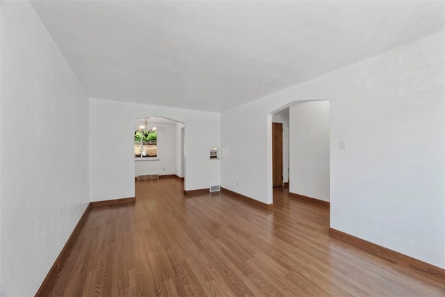 unfurnished living room featuring visible vents, arched walkways, baseboards, and wood finished floors