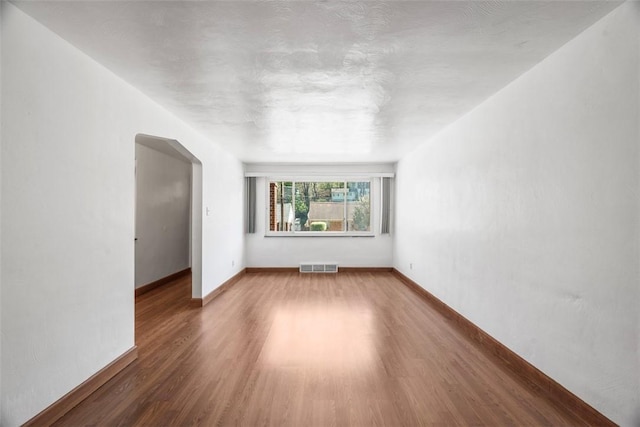 unfurnished room with arched walkways, baseboards, visible vents, and wood finished floors