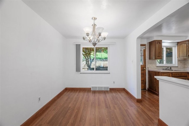 unfurnished dining area featuring a notable chandelier, visible vents, a wealth of natural light, and wood finished floors