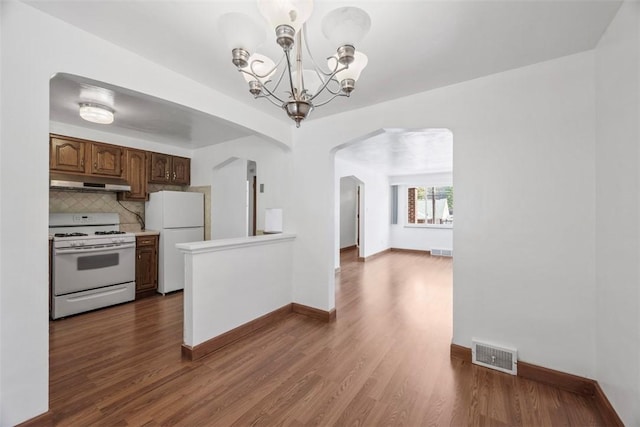 kitchen featuring white appliances, arched walkways, light countertops, under cabinet range hood, and visible vents