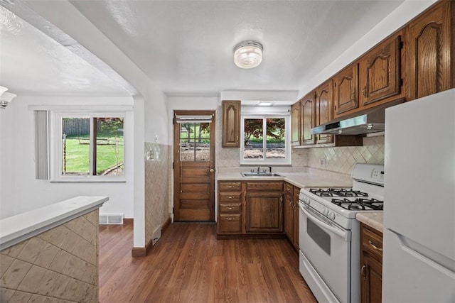 kitchen featuring visible vents, light countertops, a sink, under cabinet range hood, and white appliances