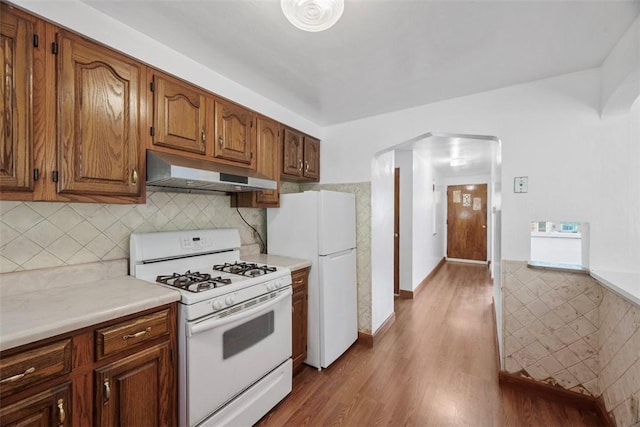 kitchen featuring under cabinet range hood, wood finished floors, white appliances, and light countertops