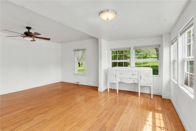 interior space featuring baseboards, a ceiling fan, light wood-type flooring, and a wealth of natural light