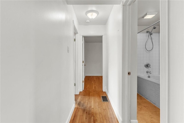 hallway with baseboards, light wood finished floors, and visible vents