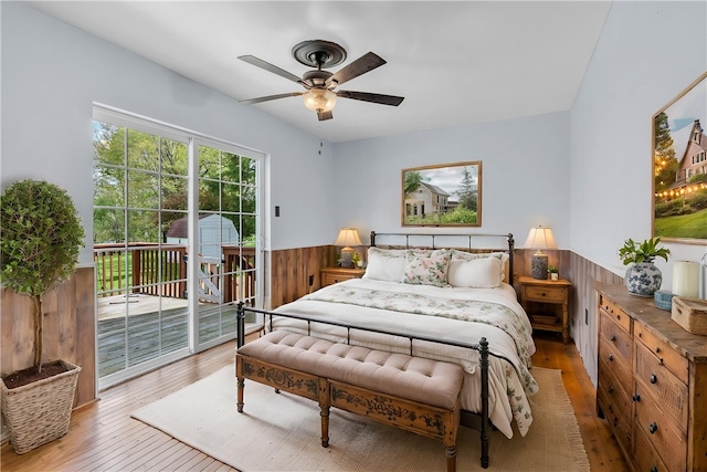 bedroom featuring access to outside, ceiling fan, light wood finished floors, and a wainscoted wall