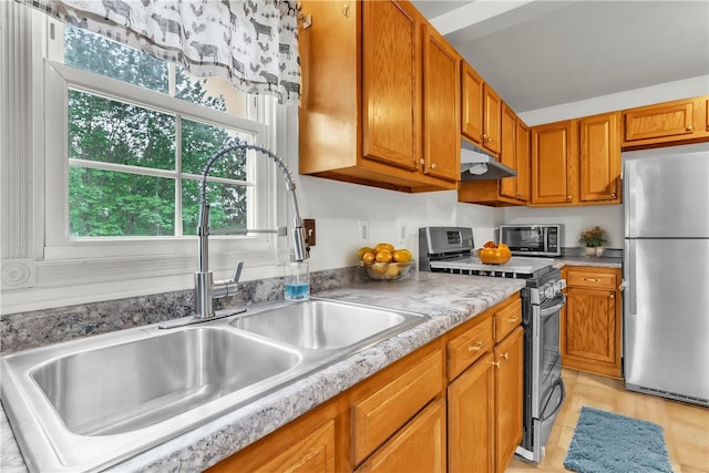 kitchen with a sink, brown cabinetry, under cabinet range hood, light countertops, and appliances with stainless steel finishes