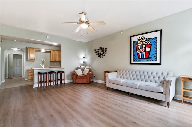 living area with arched walkways, baseboards, a ceiling fan, and light wood-type flooring